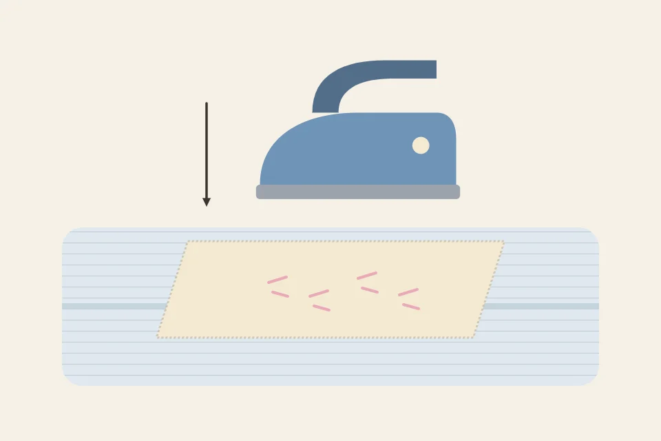 Embroidery lying face down on a folded towel with an iron held just above the back of the fabric